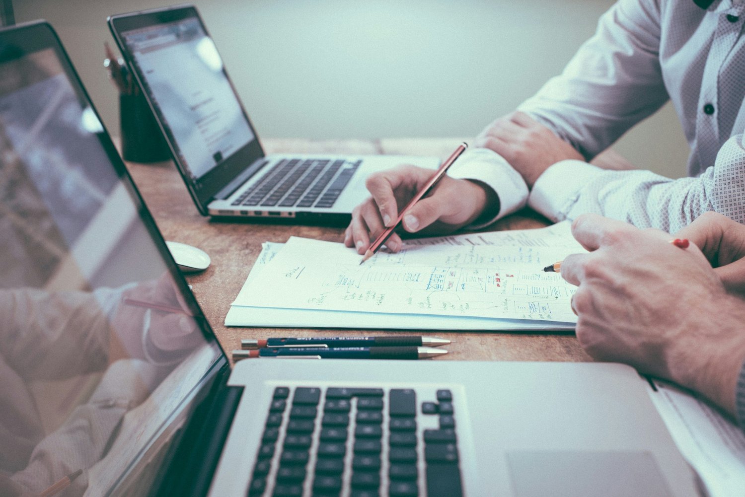 Two people working with laptops and documents on a wooden table.