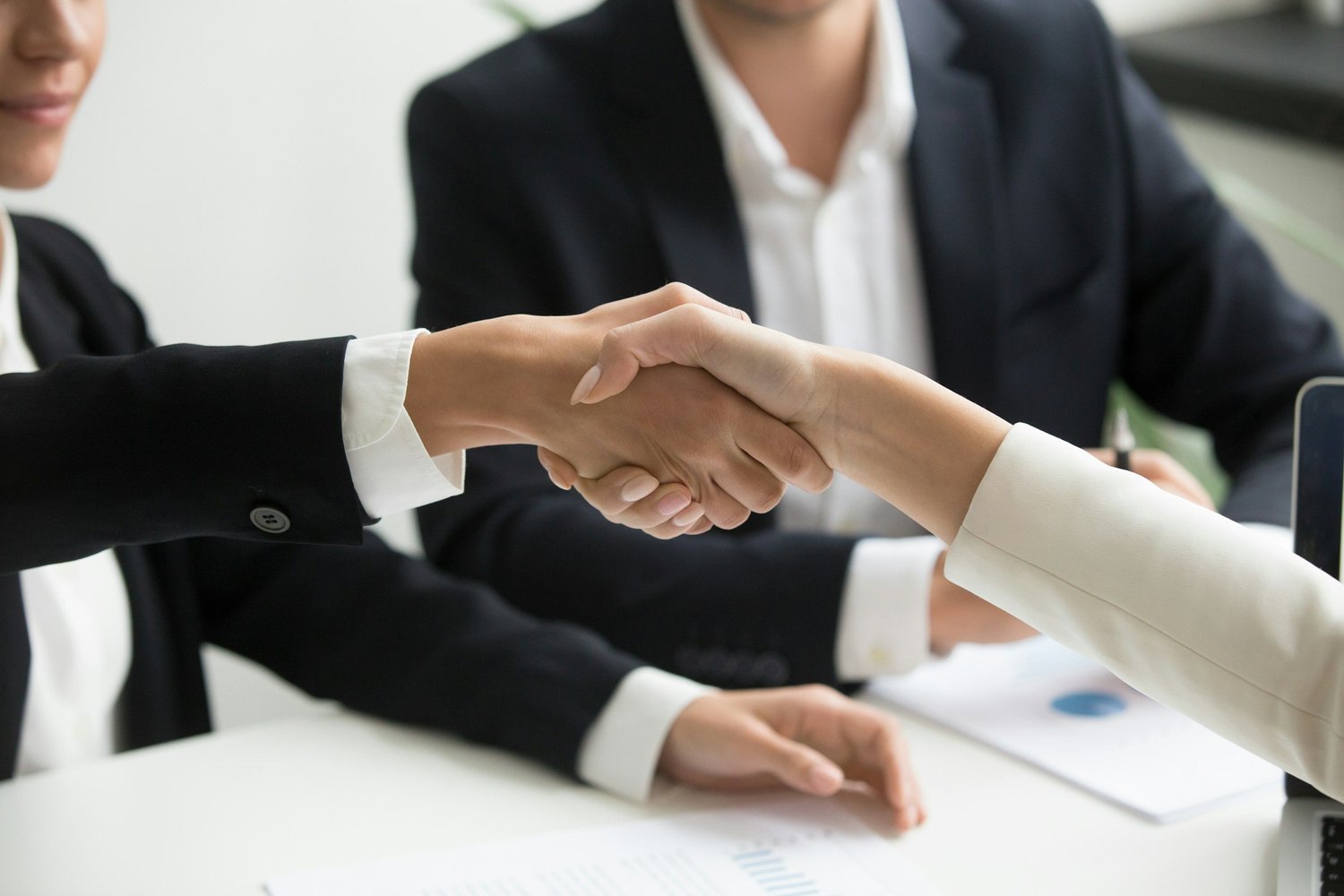 Two people in business suits shaking hands during a professional meeting.